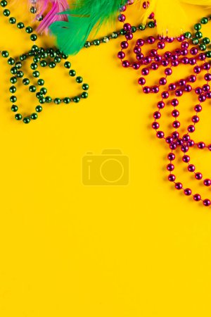 Foto de Composición de coloridas cuentas de mardi gras y plumas sobre fondo amarillo con espacio para copiar. Fiesta, celebración y concepto de carnaval. - Imagen libre de derechos