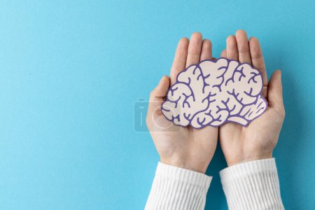 Foto de Composición de las manos sosteniendo el cerebro púrpura y blanco sobre fondo azul con espacio de copia. Servicios médicos, salud y conciencia de salud mental. - Imagen libre de derechos