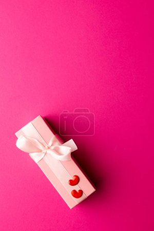 Téléchargez les photos : Vertical de boîte cadeau rose pâle avec ruban blanc et coeurs rouges, sur fond rose avec espace de copie. Saint Valentin, amour, romance et concept de célébration. - en image libre de droit