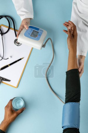 Foto de Sección media de diverso médico y paciente midiendo la presión arterial sobre fondo azul. Concepto de medicina, salud y ciencia. - Imagen libre de derechos