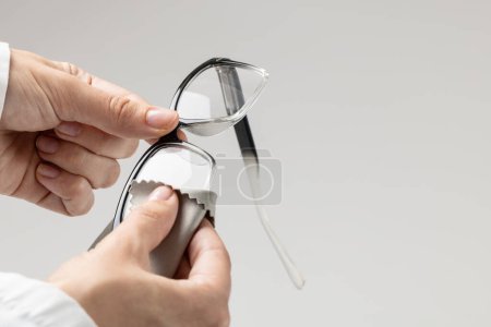Téléchargez les photos : Partie médiane du médecin caucasien tenant et nettoyant des lunettes sur fond gris. Médecine, santé et science concept. - en image libre de droit