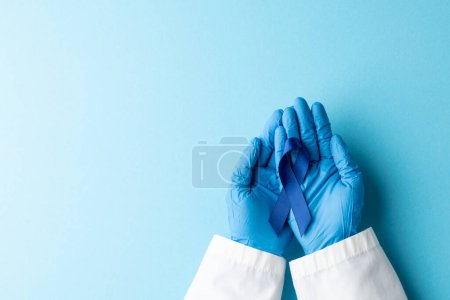 Téléchargez les photos : Mains de médecin portant des gants médicaux tenant un ruban bleu sur fond bleu. Médecine, santé et science concept. - en image libre de droit