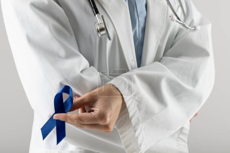 Téléchargez les photos : Partie médiane du médecin caucasien tenant un ruban bleu sur fond gris. Médecine, santé et science concept. - en image libre de droit
