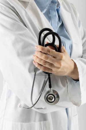 Téléchargez les photos : Partie médiane du médecin caucasien tenant un stéthoscope sur fond gris avec espace de copie. Médecine, santé et science concept. - en image libre de droit