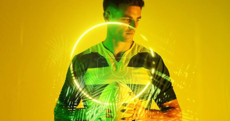 Photo for Caucasian thoughtful male player holding rugby ball over illuminated circle and plants. Yellow, serious, copy space, composite, sport, competition, shape, nature and abstract concept. - Royalty Free Image