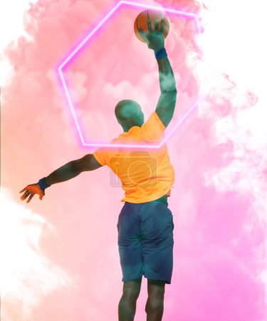 Téléchargez les photos : Vue arrière du joueur afro-américain prenant un tir avec le basket-ball par hexagone sur fond fumé. Composite, chauve, espace de copie, rose, sport, compétition, illustration, illuminé, concept de forme. - en image libre de droit