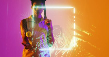 Photo for Biracial female tennis player with racket and ball standing by illuminated square and plants. Copy space, composite, sport, competition, match, nature, shape and abstract concept, - Royalty Free Image