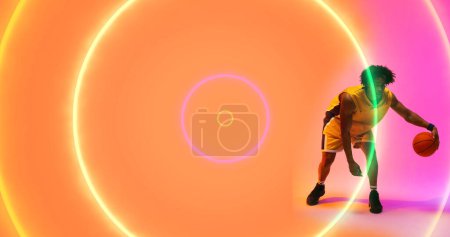 Photo for Composite of biracial basketball player dribbling ball by illuminated multicolored circles. Copy space, sport, competition, illustration, glowing, shape and abstract concept. - Royalty Free Image