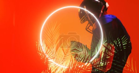Téléchargez les photos : Joueur de football américain portant un casque et tenant le ballon par cercle éclairé et des plantes. Orange, espace de copie, composite, sport, compétition, illustration, lueur, nature, concept de forme. - en image libre de droit