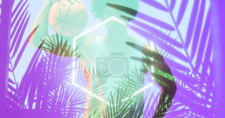 Téléchargez les photos : Composite d'hexagone éclairé et de plantes sur un joueur masculin biracial tenant du basket-ball. Sport, compétition, illustration, éclat, nature, forme et concept abstrait. - en image libre de droit