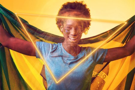 Téléchargez les photos : Néon hexagonal sur heureuse fan afro-américaine avec drapeau pendant le match de football. Composite numérique, fond jaune, drapeau brésilien, sport, spectateur, amour, victoire, succès. - en image libre de droit