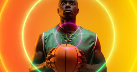 Foto de Compuesto de círculos iluminados sobre jugador de baloncesto afroamericano con pelota mirando hacia arriba. Espacio serio, copia, deporte, competición, ilustración, forma y concepto abstracto. - Imagen libre de derechos