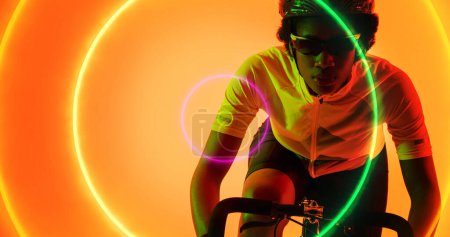 Téléchargez les photos : Athlète féminine Biracial portant des lunettes et un casque à vélo sur des cercles colorés éclairés. Composite, espace de copie, sport, cyclisme, course, compétition, forme et concept abstrait. - en image libre de droit