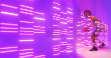 Téléchargez les photos : Composite de joueur de basket-ball biracial dribble par des lumières éclairées sur fond violet. Copier l'espace, le sport, la compétition, l'illustration, le rayonnement, la forme et le concept abstrait. - en image libre de droit