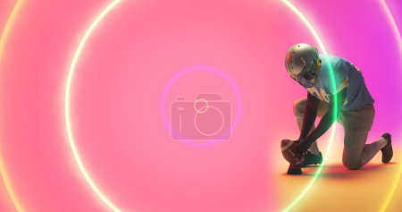 Foto de Compuesto de círculos iluminados de colores y jugador de fútbol americano jugando sobre fondo rosa. Copiar el espacio, el deporte, la competencia, el neón, la ilustración, el brillo, la bola y el concepto abstracto. - Imagen libre de derechos