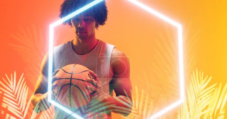 Photo for Thoughtful biracial basketball player with afro hair holding ball by illuminated hexagon and plants. Copy space, composite, sport, competition, illustration, glowing, nature, shape and abstract. - Royalty Free Image