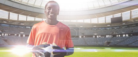 Foto de Retrato del joven portero afroamericano sonriente con pelota en el campo de fútbol, espacio para copiar. Deporte, deporte competitivo, habilidad, atleta, partido, panorámica, retroiluminado. - Imagen libre de derechos
