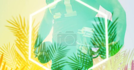 Téléchargez les photos : Milieu du joueur de football tenant ballon et casque sur hexagone éclairé et plantes. - en image libre de droit