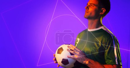 Photo for Caucasian young soccer player holding ball by geometric neon design over blue background, copy space. Computer graphic, digital composite, soccer, design, athlete, competitive sport. - Royalty Free Image