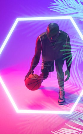 Téléchargez les photos : Basketteur chauve afro-américain jonglant avec la balle par hexagone éclairé et plantes. Copier l'espace, composite, sport, compétition, illustration, lumineux, concept de nature et de forme. - en image libre de droit