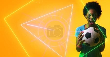 Photo for Biracial female soccer player with brazilian flag's face paint screaming over geometric shapes. Illuminated, copy space, composite, sport, competition, cheerful, ball, mouth open, patriotism. - Royalty Free Image