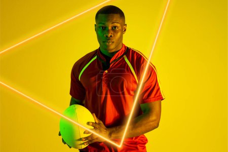 Photo for Triangle neon over confident african american young rugby player holding ball on yellow background. Digital composite, sport, rugby, athlete, competitive sport, skill, copy space, portrait. - Royalty Free Image