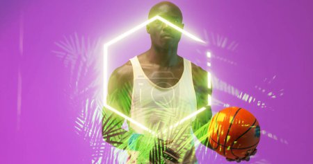Téléchargez les photos : Portrait d'un joueur de basket-ball afro-américain chauve tenant le ballon par un hexagone lumineux et des plantes. Composite, violet, sérieux, espace de copie, sport, compétition, illustration, illuminé, nature, forme. - en image libre de droit