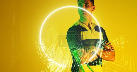 Photo for Thoughtful caucasian rugby player with arms crossed by circle and plants on yellow background. Copy space, composite, sport, competition, shape, nature, looking away and abstract concept. - Royalty Free Image
