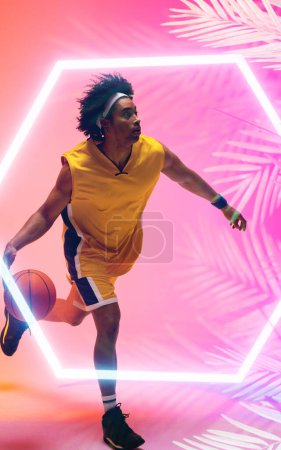Photo for Composite of biracial basketball player dribbling ball by illuminated hexagon and plants, copy space. Pink, sport, competition, illustration, glowing, nature and shape concept. - Royalty Free Image