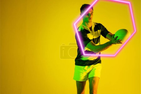 Photo for Caucasian male rugby player catching ball by illuminated hexagon over yellow background. Copy space, composite, sport, competition, shape, playing, match and abstract concept. - Royalty Free Image