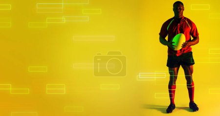 Foto de Jugador de rugby afroamericano sosteniendo pelota por coloridos rectángulos sobre fondo amarillo, espacio de copia. Compuesto, deporte, competición, juego, partido, retrato, forma y concepto abstracto. - Imagen libre de derechos