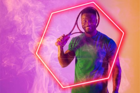 Téléchargez les photos : Un joueur de tennis afro-américain souriant tenant une raquette par un hexagone illuminé au milieu de la fumée. Espace de copie, composite, sport, forme, compétition, jeu, match et concept abstrait. - en image libre de droit