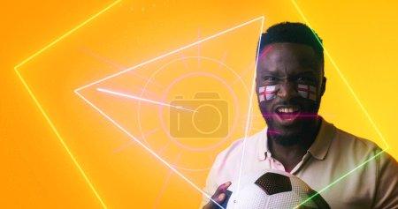 Photo for African american soccer player with english flag's face paint holding ball by geometric shapes. Portrait, yellow, sport, competition, screaming, illuminated, shape, patriotism and abstract concept. - Royalty Free Image