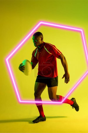 Téléchargez les photos : Joueur afro-américain de rugby masculin avec balle exécutée par hexagone illuminé sur fond vert. Espace de copie, composite, sport, compétition, forme, jeu, match et concept abstrait. - en image libre de droit