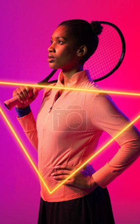 Photo for African american female tennis player with hand on hip holding racket by illuminated triangle. Copy space, composite, sport, competition, shape, contemplation, match and abstract concept. - Royalty Free Image