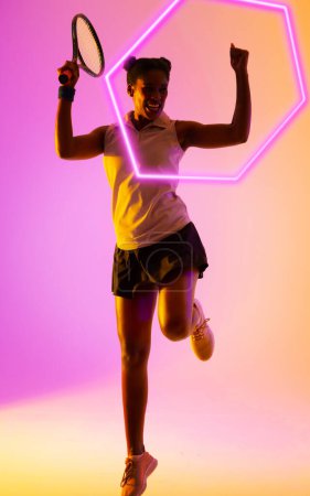Photo for Excited african american tennis player holding racket and raising hands by illuminated hexagon. Copy space, composite, celebration, sport, shape, competition, winner, match and abstract concept. - Royalty Free Image