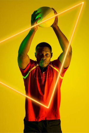 Photo for African american male rugby player throwing ball over illuminated triangle on yellow background. Copy space, composite, sport, competition, shape, playing, match and abstract concept. - Royalty Free Image