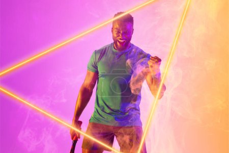 Photo for African american male tennis player with racket shaking fist and screaming by illuminated triangle. Copy space, composite, sport, shape, celebration, winner, competition, match and abstract concept. - Royalty Free Image