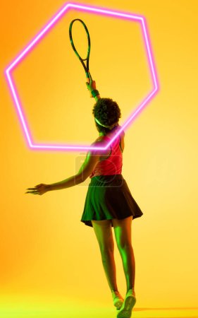 Téléchargez les photos : Vue arrière du joueur de tennis afro-américain avec raquette et hexagone illuminé sur fond jaune. Espace de copie, composite, sport, compétition, jeu, match et concept abstrait. - en image libre de droit