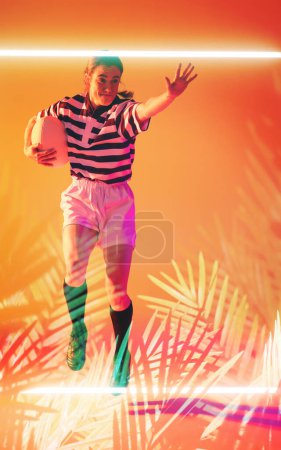 Foto de Jugadora de rugby caucásica con pelota saltando sobre rectángulo iluminado y plantas. Copiar espacio, compuesto, deporte, competencia, forma, naturaleza, juego, partido y concepto abstracto. - Imagen libre de derechos
