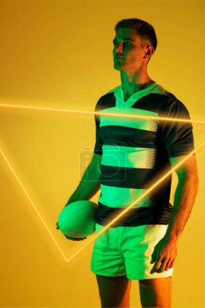 Téléchargez les photos : Joueur de rugby masculin caucasien tenant la balle et debout par triangle illuminé sur fond jaune. Espace de copie, confiant, composite, sport, forme, compétition, jeu, match et concept abstrait. - en image libre de droit