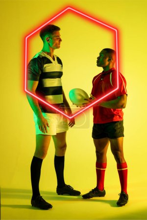 Téléchargez les photos : Des adversaires masculins multiraciaux de rugby se regardent en s'illuminant d'hexagone sur fond jaune. Copier l'espace, composite, forme, sport, compétition, balle, jeu, match et concept abstrait. - en image libre de droit
