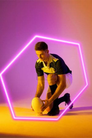 Photo for Caucasian male rugby player placing ball on stand by illuminated hexagon over gradient background. Copy space, composite, sport, shape, competition, playing, match and abstract concept. - Royalty Free Image
