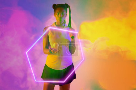 Photo for Confident african american female tennis player with racket and ball by illuminated hexagon. Copy space, composite, sport, shape, competition, smoke, playing, match and abstract concept. - Royalty Free Image