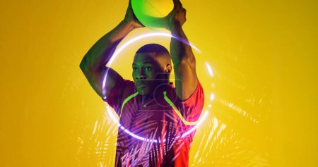 Photo for African american rugby player holding ball looking away by illuminated plants and circle. Yellow, copy space, composite, sport, competition, shape, nature, playing, match and abstract concept. - Royalty Free Image