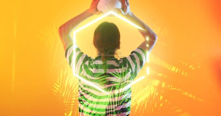 Photo for Illuminated hexagon and plants over rear view of caucasian female rugby player throwing ball. Copy space, composite, sport, competition, shape, nature, playing, match and abstract concept. - Royalty Free Image