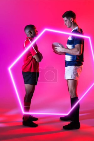 Téléchargez les photos : Des adversaires masculins multiraciaux de rugby se fixent l'un l'autre par un hexagone illuminé sur fond rose. Copier l'espace, composite, sport, forme, balle, compétition, jeu, match et concept abstrait. - en image libre de droit