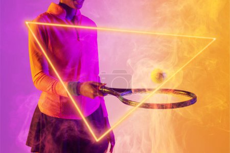 Photo for Midsection of african american female player playing with racket and ball by illuminated triangle. Copy space, composite, tennis, sport, shape, smoke, hand, competition, match and abstract concept. - Royalty Free Image