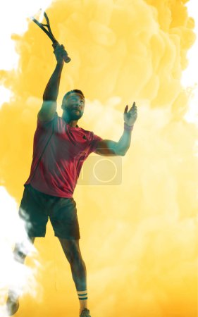Photo for African american male tennis player hitting with racket over yellow smoky background. Copy space, composite, sport, competition, playing, match and abstract concept. - Royalty Free Image