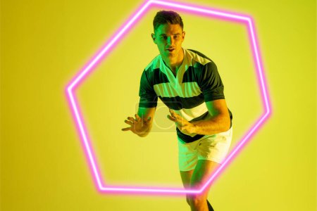 Photo for Caucasian male rugby player standing by illuminated hexagon over yellow background. Copy space, composite, sport, shape, competition, playing, match and abstract concept. - Royalty Free Image